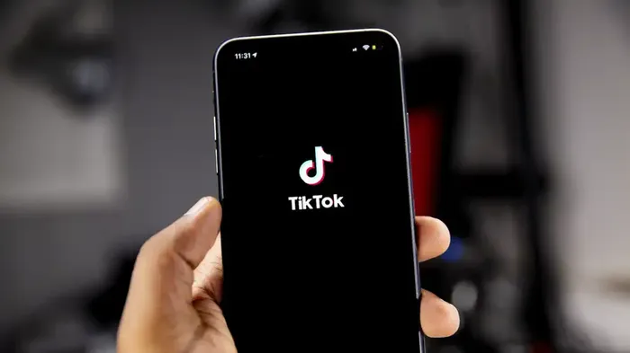 Bilde av en h?nd som holder en telefon med tiktok-logoen p? skjermen